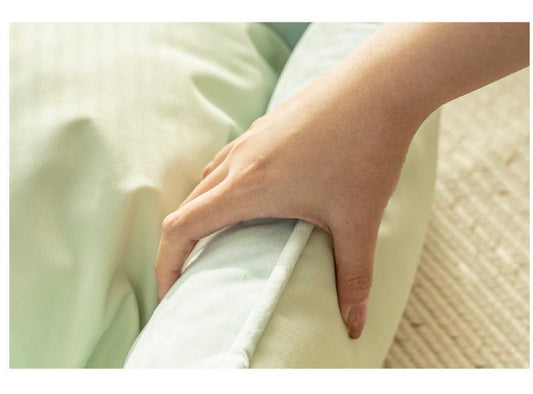 Hand gripping a light green fabric cushion on a beige textured rug