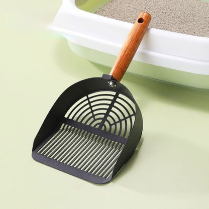 Black metal cat litter scoop with wooden handle next to white litter box filled with clumping cat litter