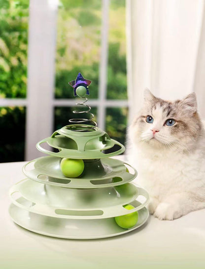 Fluffy cat with blue eyes next to a green multi-level cat ball track toy with star topper