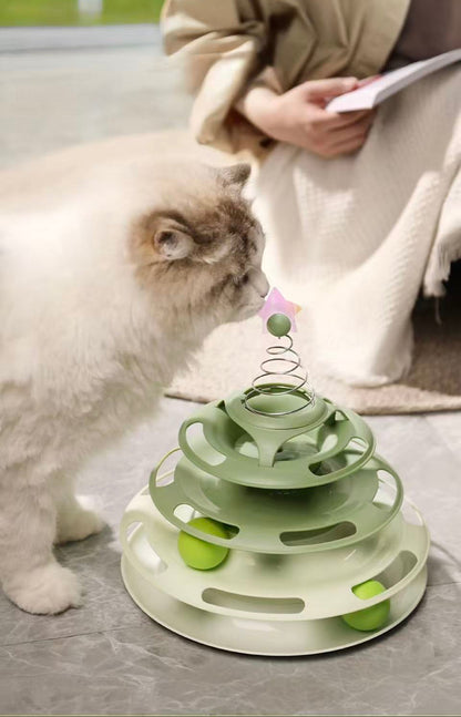 Fluffy white and gray cat playing with a green multi-tiered interactive ball toy indoors