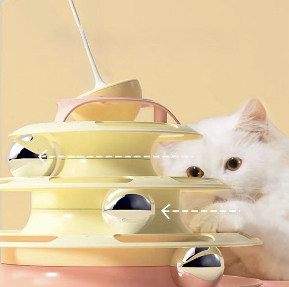 White cat playing with yellow and pink multi-level cat toy with silver balls on beige background