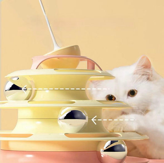 White cat playing with yellow and pink multi-level cat toy with silver balls on beige background