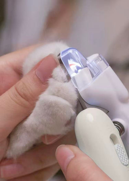 Person trimming a white cat's claw using a white pet nail clipper with protective cover