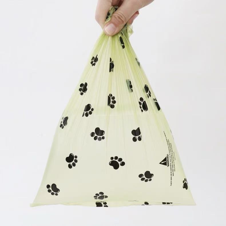Hand holding a translucent yellow pet waste bag with black paw print pattern