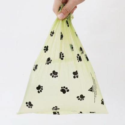 Hand holding a translucent yellow pet waste bag with black paw print pattern