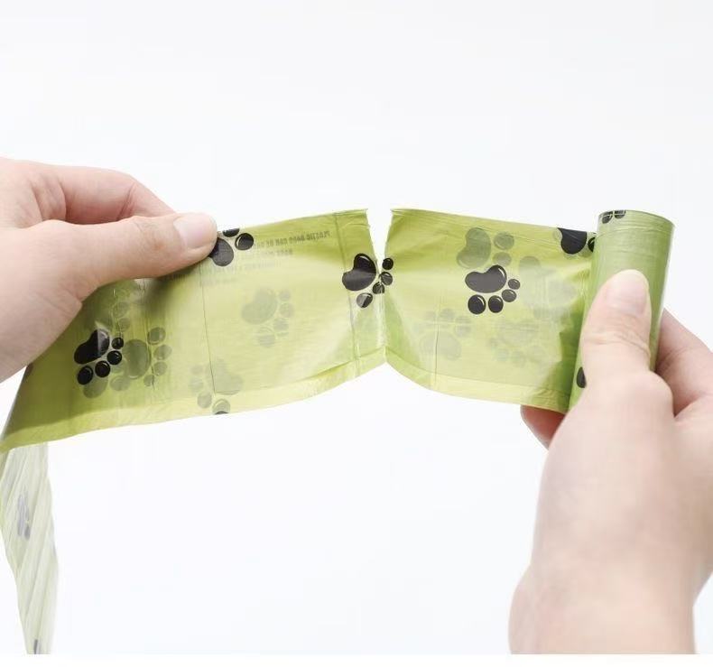 Hands tearing a green dog waste bag roll with black paw print patterns against white background